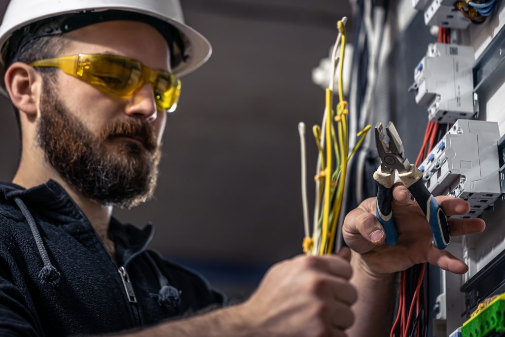 electrician wearing safety gear while wiring an electrical switchboard