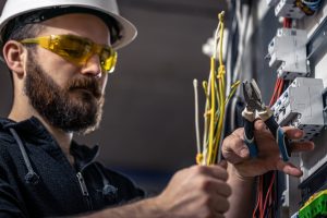 electrician wearing safety gear while wiring an electrical switchboard